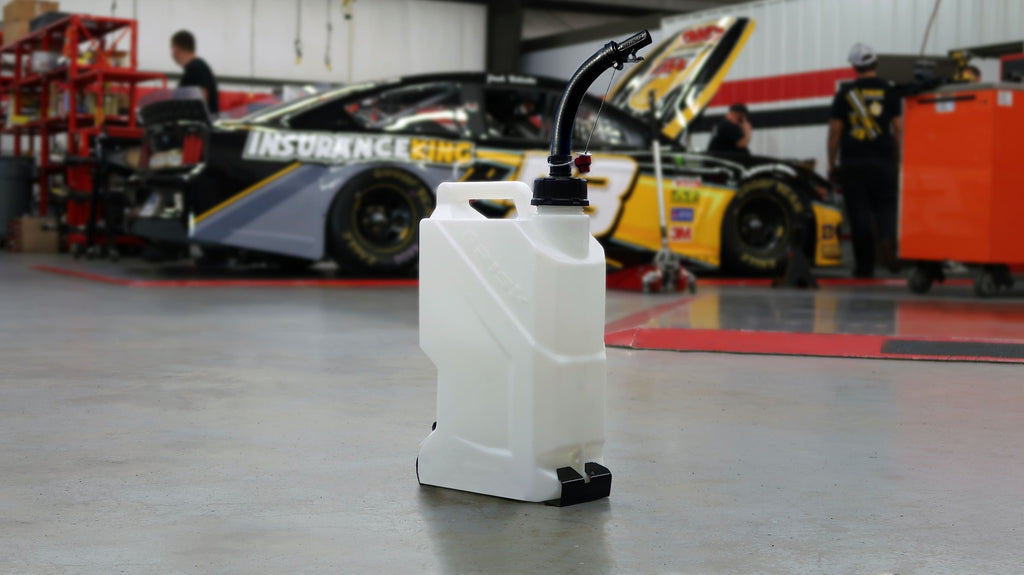White fuel tank with black nozzle on a garage floor with racing cars in the background
