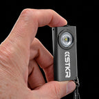 Gray STKR SlimJIMMY keychain light held between two fingers to show its size