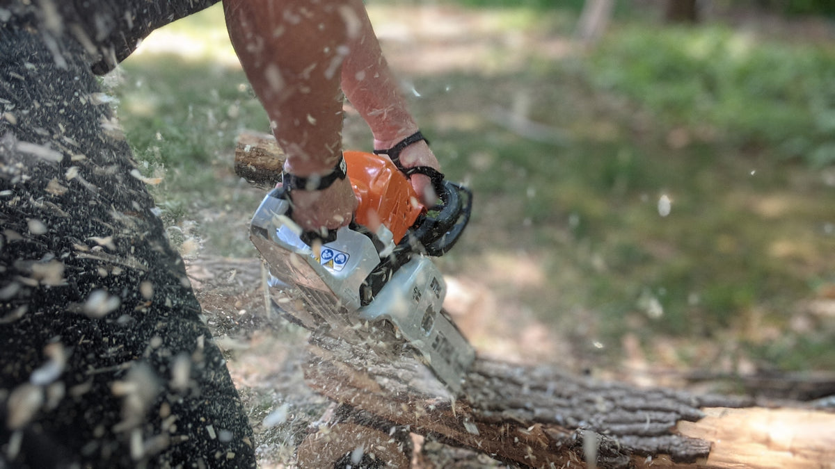 Palm Protectors worn while cutting a log with a chainsaw, wood chips flying